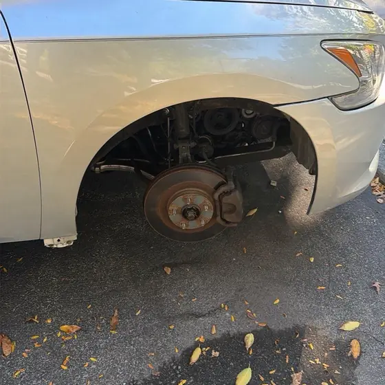 Silver Nissan parked at the curb with its front wheel off and the brake rotor showing